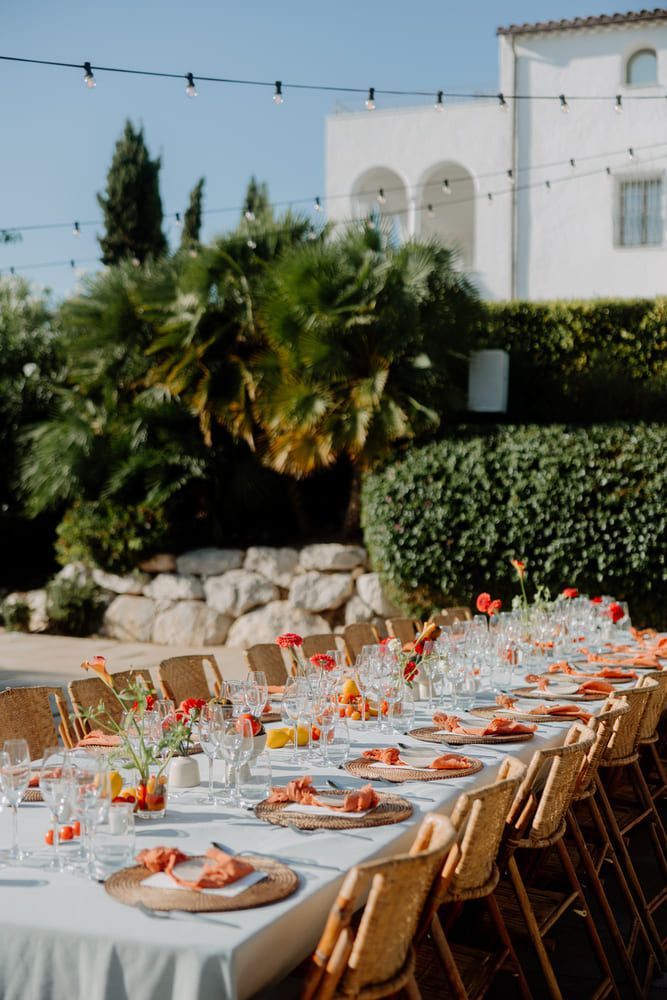 Mesa de recepción de boda al aire libre con flores y decoración de color naranja, sillas de mimbre.