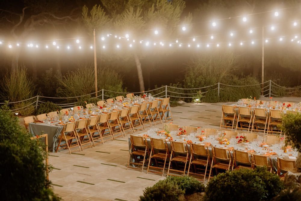 Recepción de boda al aire libre, mesas preparadas, luces colgadas en el techo, sillas doradas.