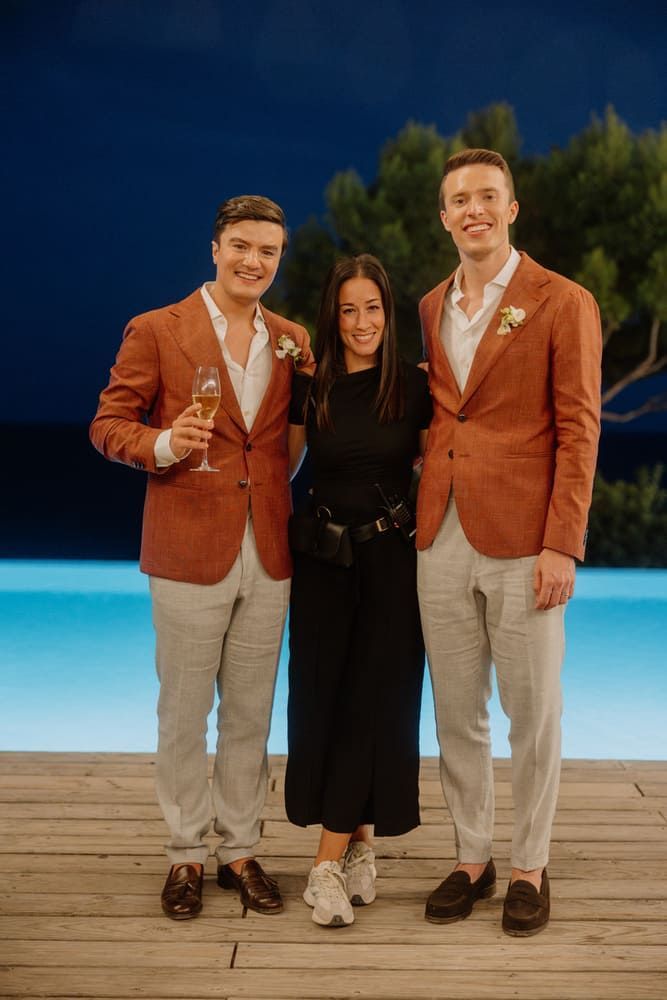 Tres personas: dos hombres con blazers de color naranja quemado y una mujer sonriente junto a una piscina.