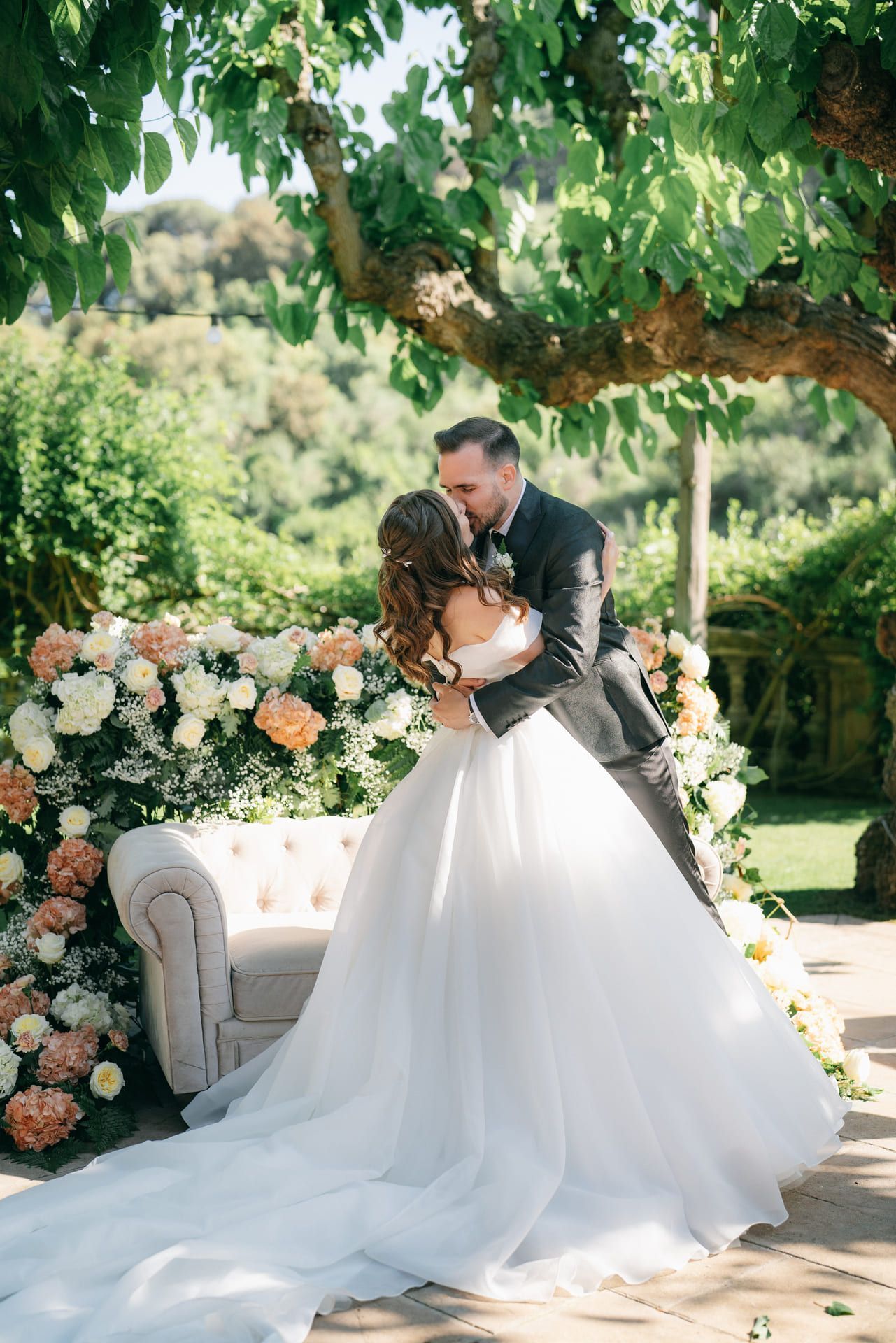 Pareja besándose con traje de boda, un arco floral y un entorno de jardín.