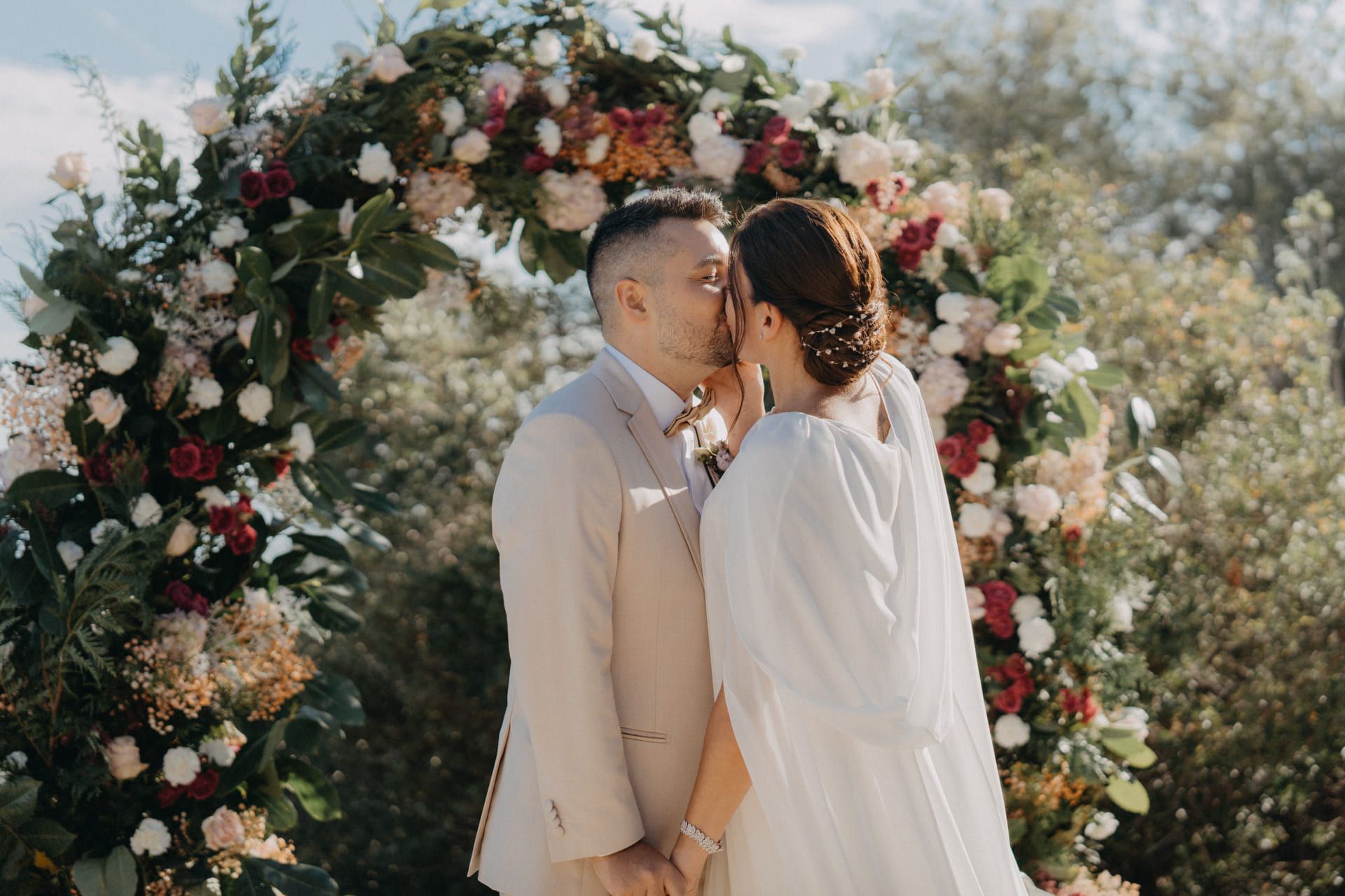 Pareja besándose bajo un arco floral en una ceremonia de boda al aire libre.