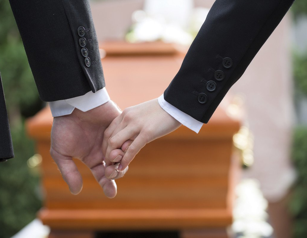 Deux personnes se tiennent la main devant un cercueil