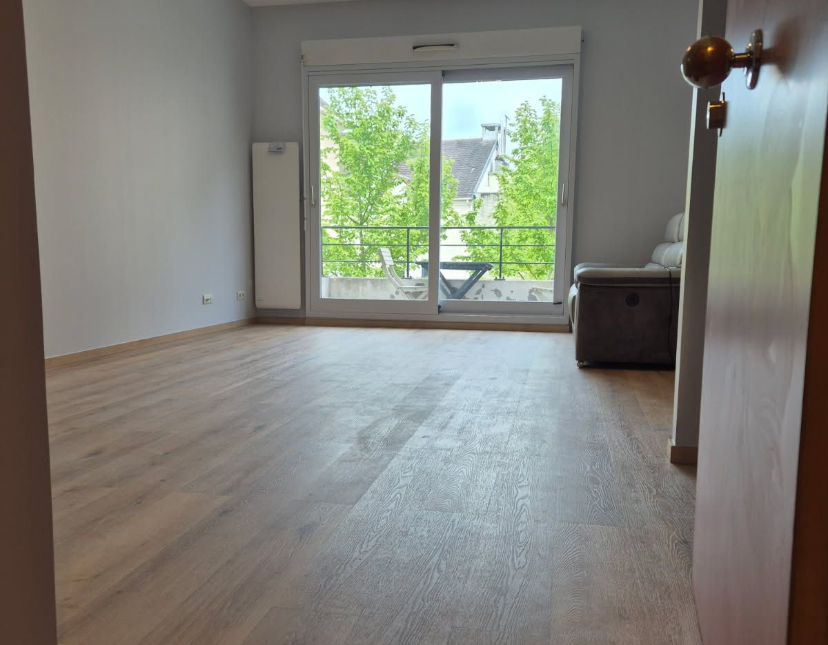 Pièce vide avec parquet clair et baie vitrée.