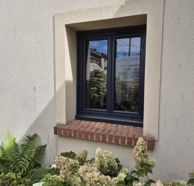 Fenêtre à cadre foncé et appui en brique encastrée dans un mur en stuc.