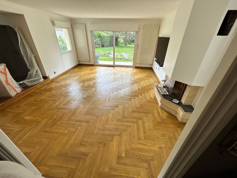 Un salon lumineux avec parquet à chevrons, cheminée et grandes fenêtres.