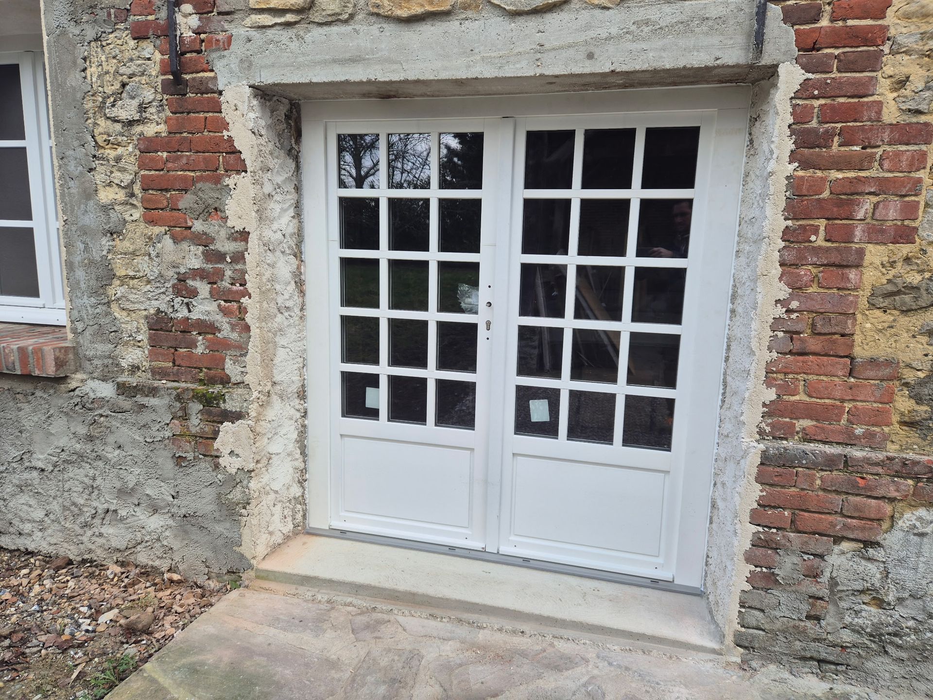 Portes-fenêtres blanches encastrées dans un bâtiment en briques et en pierres patinées par le temps.