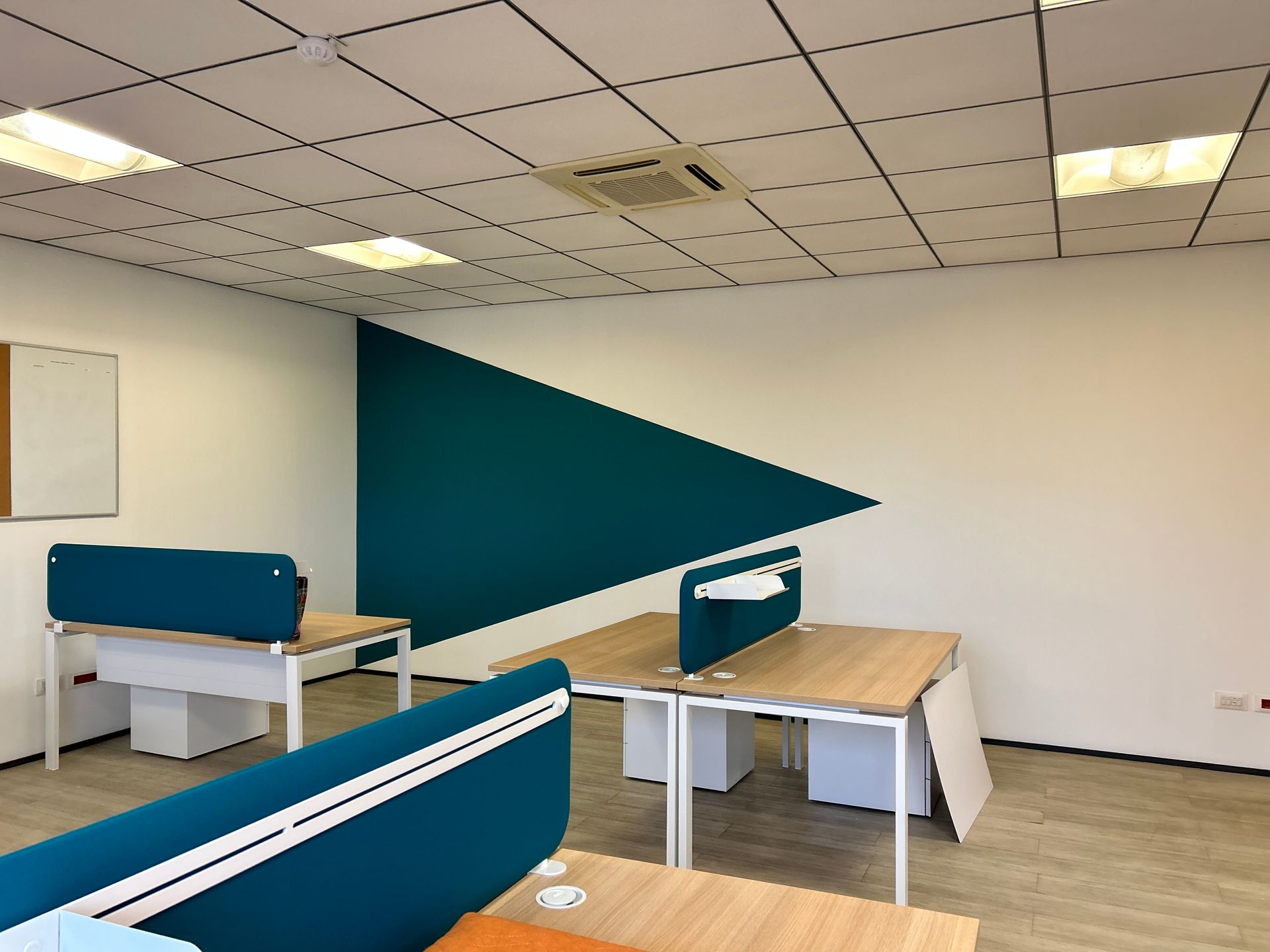 Espace de bureau avec un triangle turquoise peint sur un mur blanc, des bureaux et des cloisons.