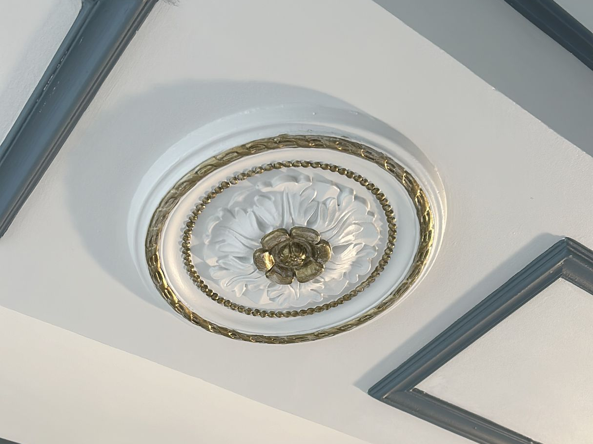 Moulure de plafond blanche avec bordure et éléments décoratifs dorés.