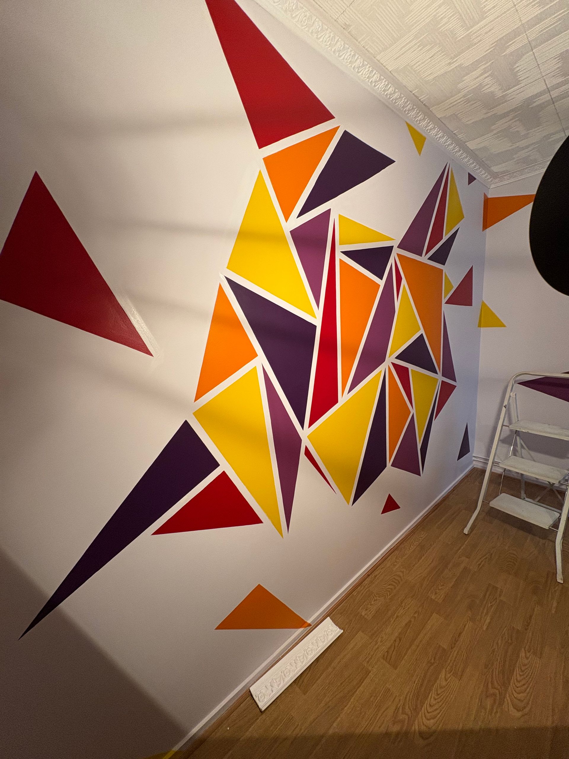 Fresque murale colorée en forme de triangle géométrique sur un mur blanc.