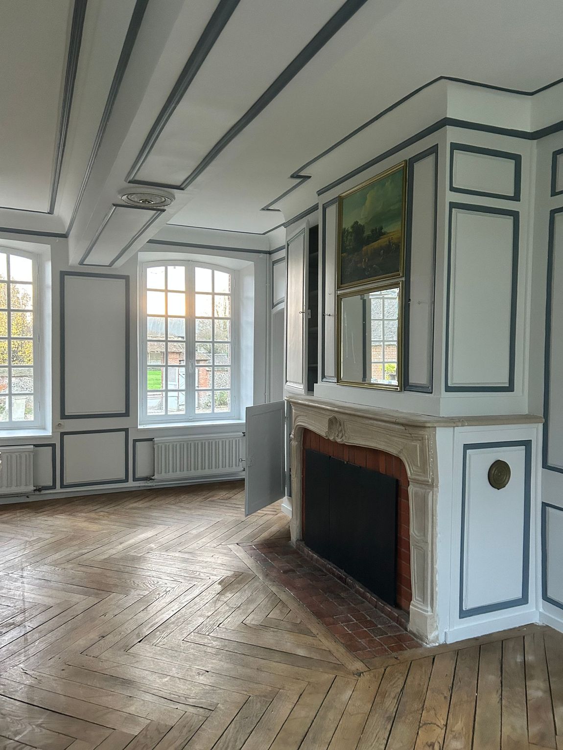Pièce ornée avec cheminée, fenêtres et panneaux muraux décoratifs dans un bâtiment avec du parquet.