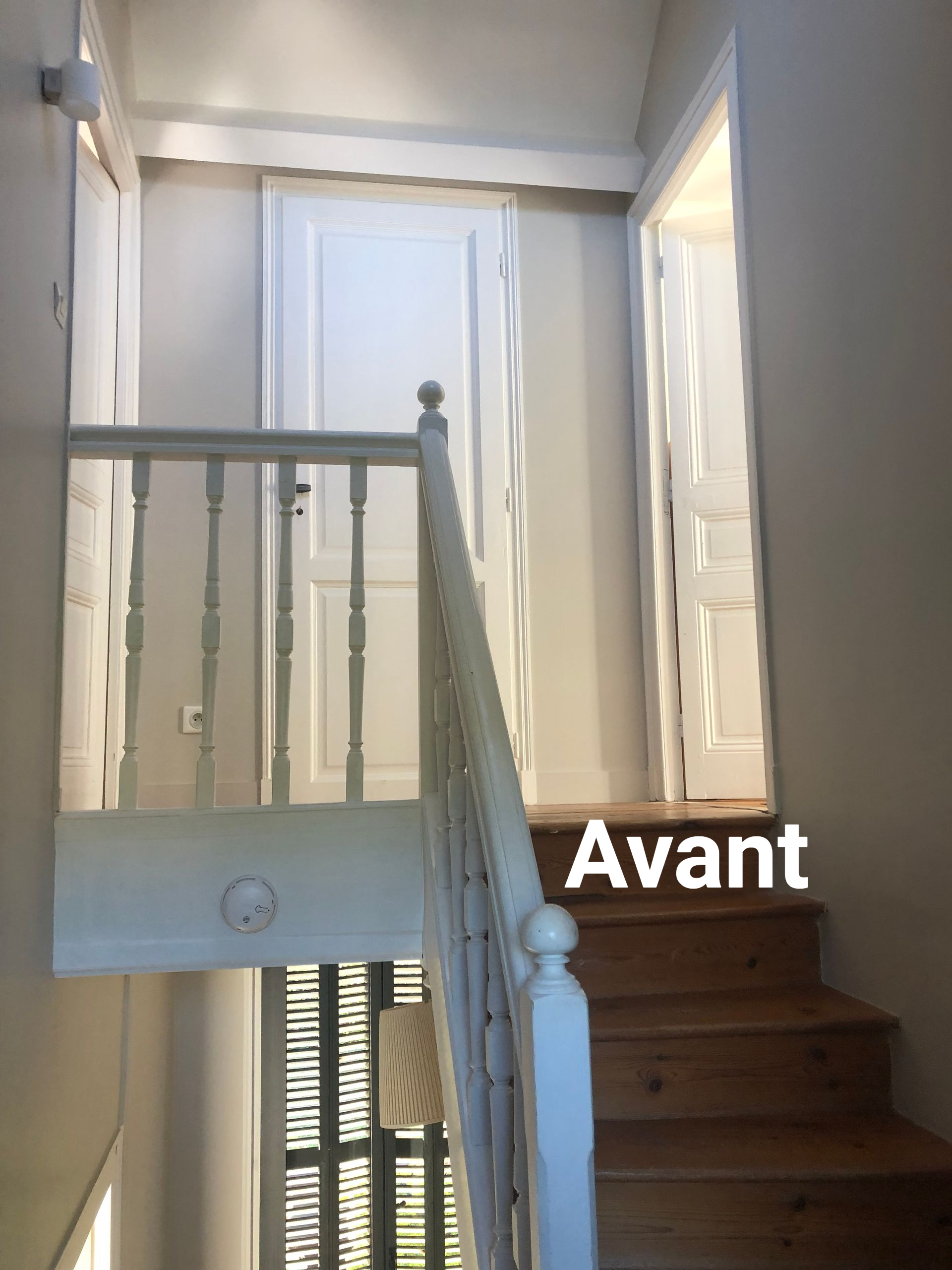 Escalier en bois menant à l'étage, rampe blanche, portes sur le palier.