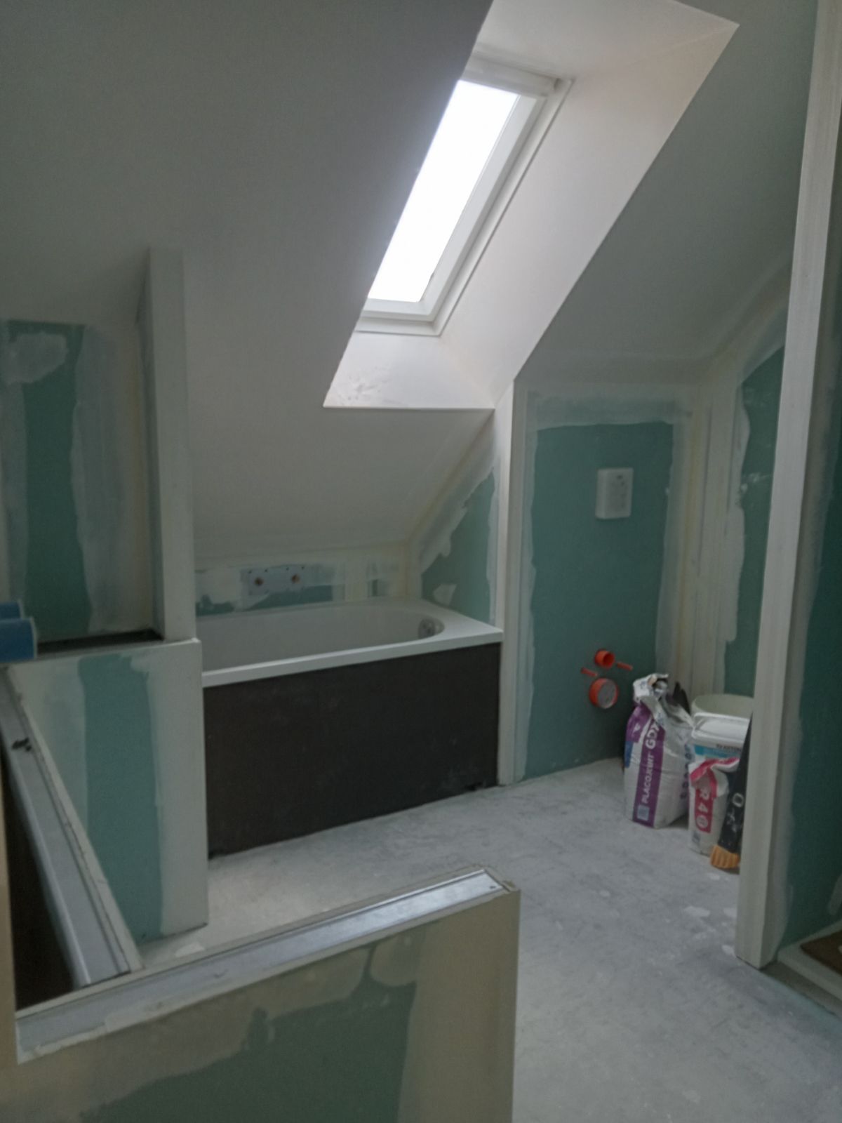 Création d'une salle de bains : cloisons en plaque de plâtre posées, baignoire installée.