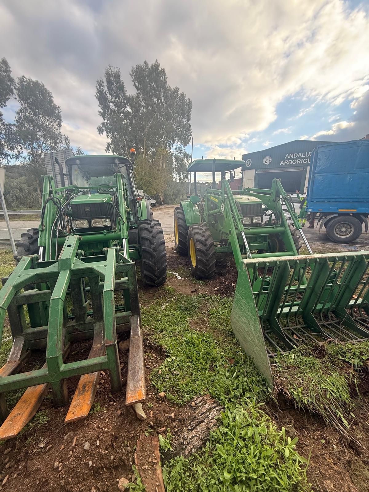Maquinaria agrícola alineada en un campo embarrado, con tractores e implementos verdes bajo un cielo nublado