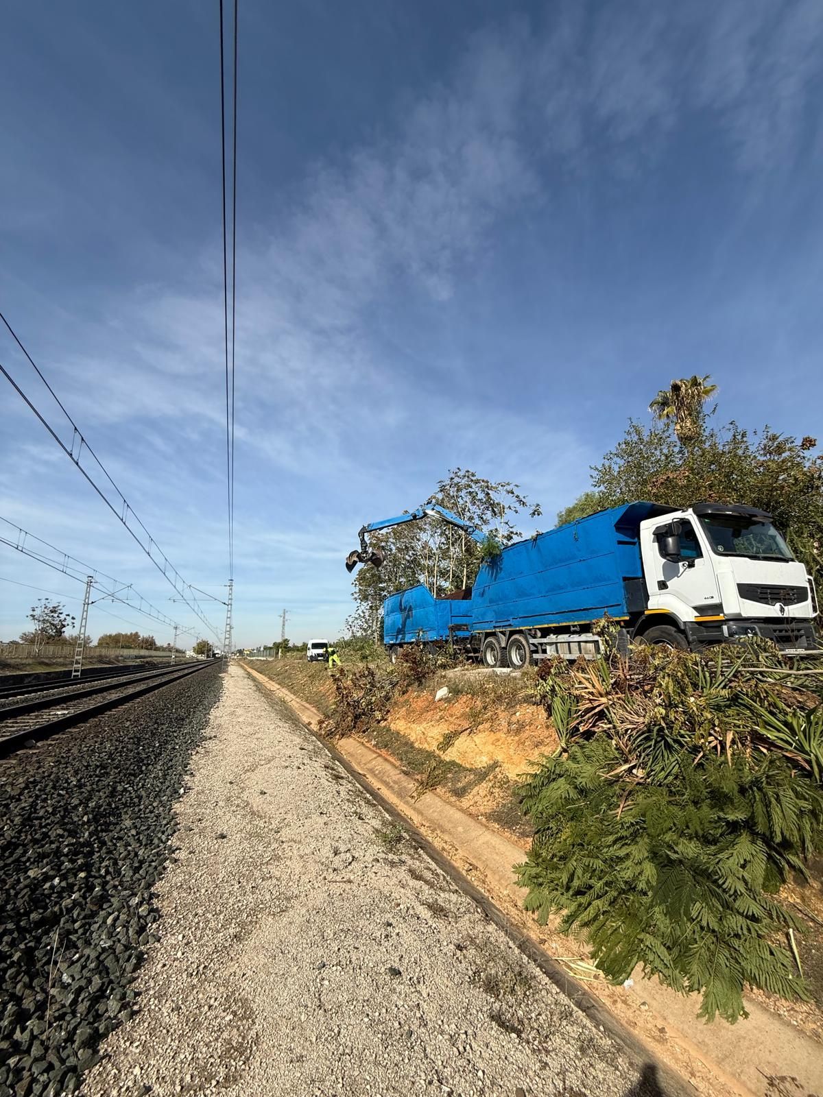 Locomotora azul sobre las vías, junto a una vía férrea de grava, bajo un cielo despejado