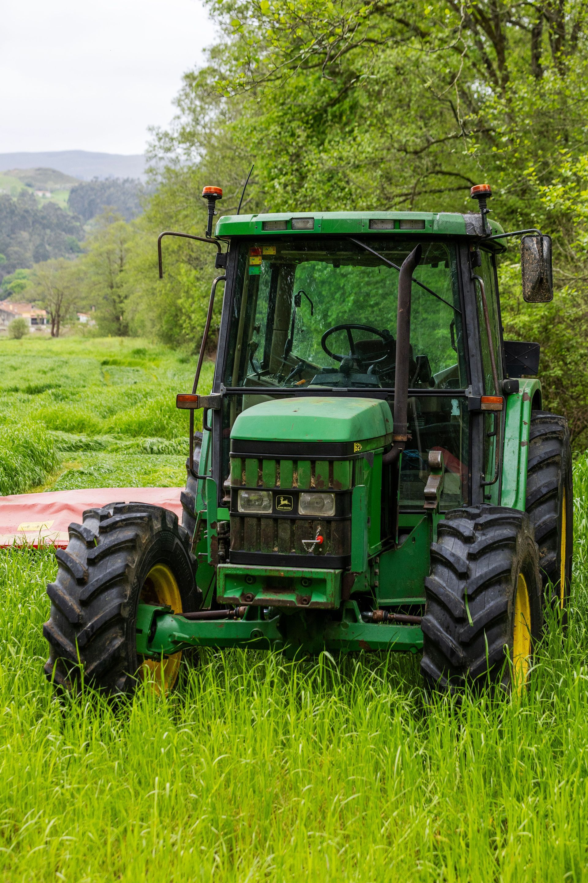 Tractor verde en un campo de hierba con árboles al fondo