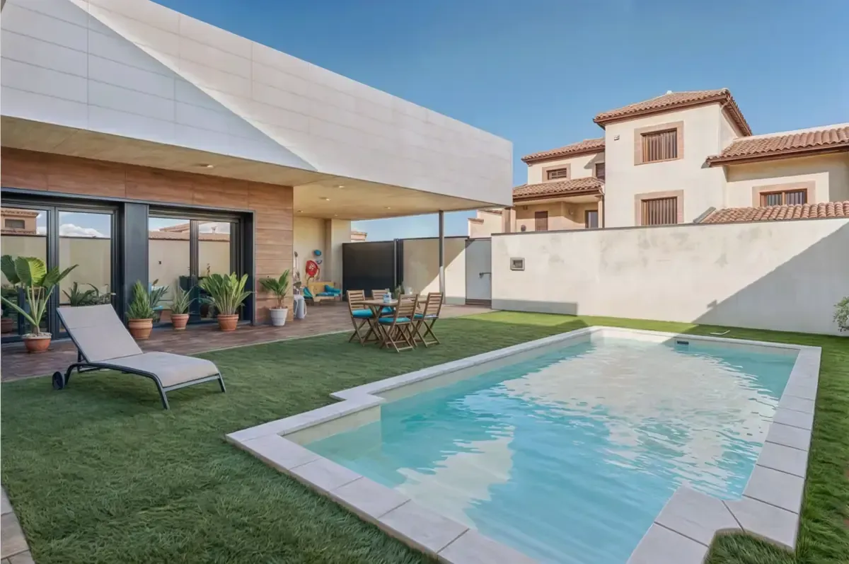 Patio trasero con piscina, muebles de patio y una casa moderna bajo un cielo azul claro.