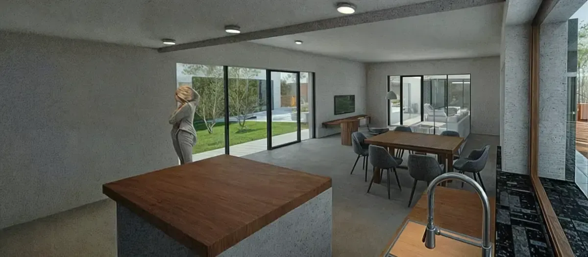 Interior moderno con una persona cerca de una ventana grande, isla de cocina y área de comedor con mesa y sillas.