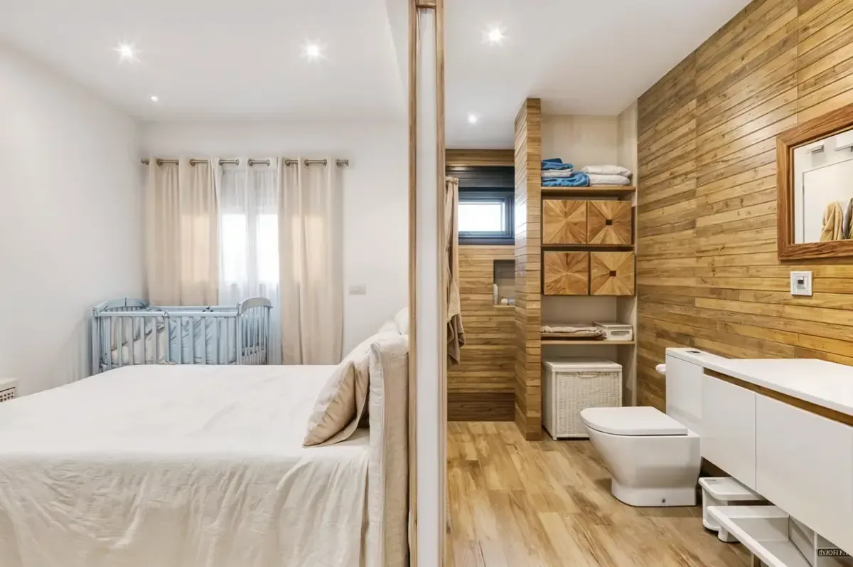 Dormitorio con cama y cuna, abierto a un baño con paredes de madera, inodoro y tocador.