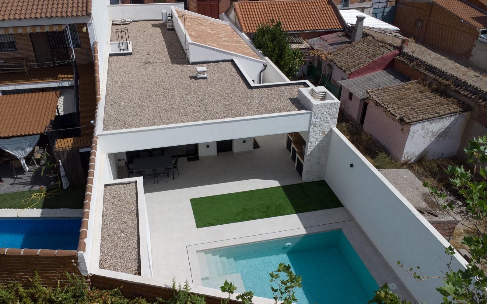 Vista aérea de una casa moderna con piscina, patio y césped artificial. Exterior blanco con techo plano.
