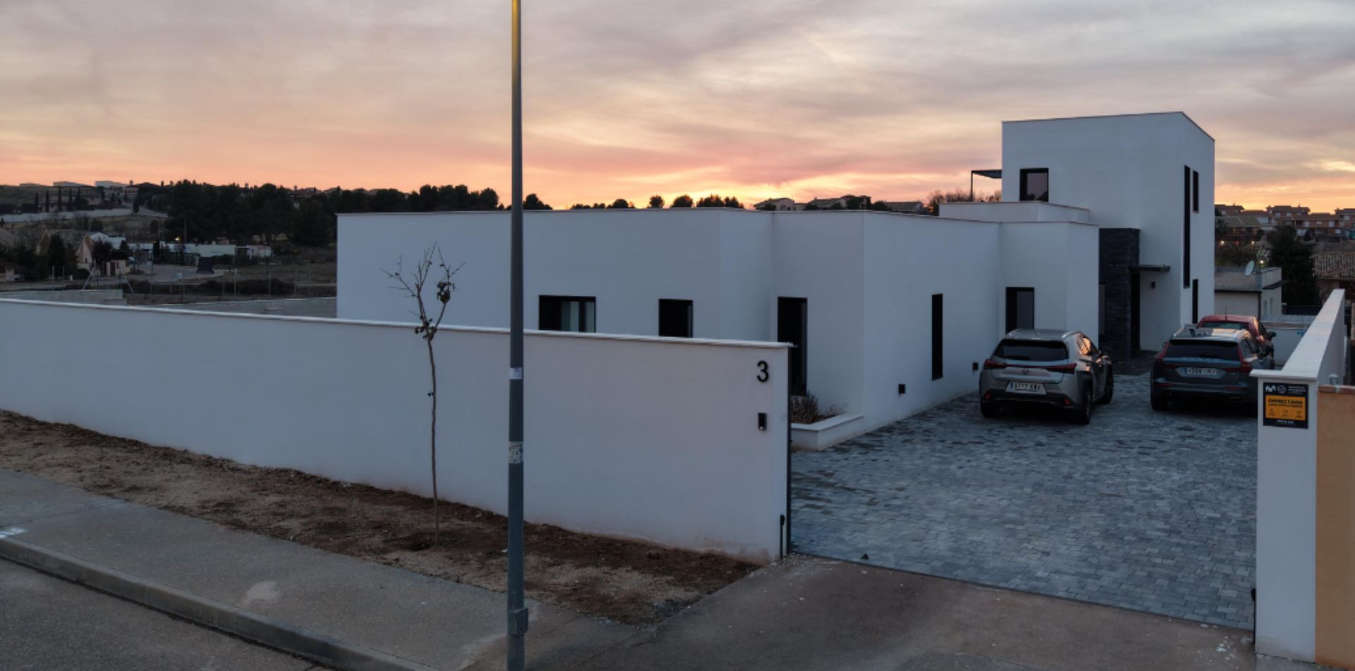Moderna casa blanca con coches aparcados en frente durante la puesta de sol.