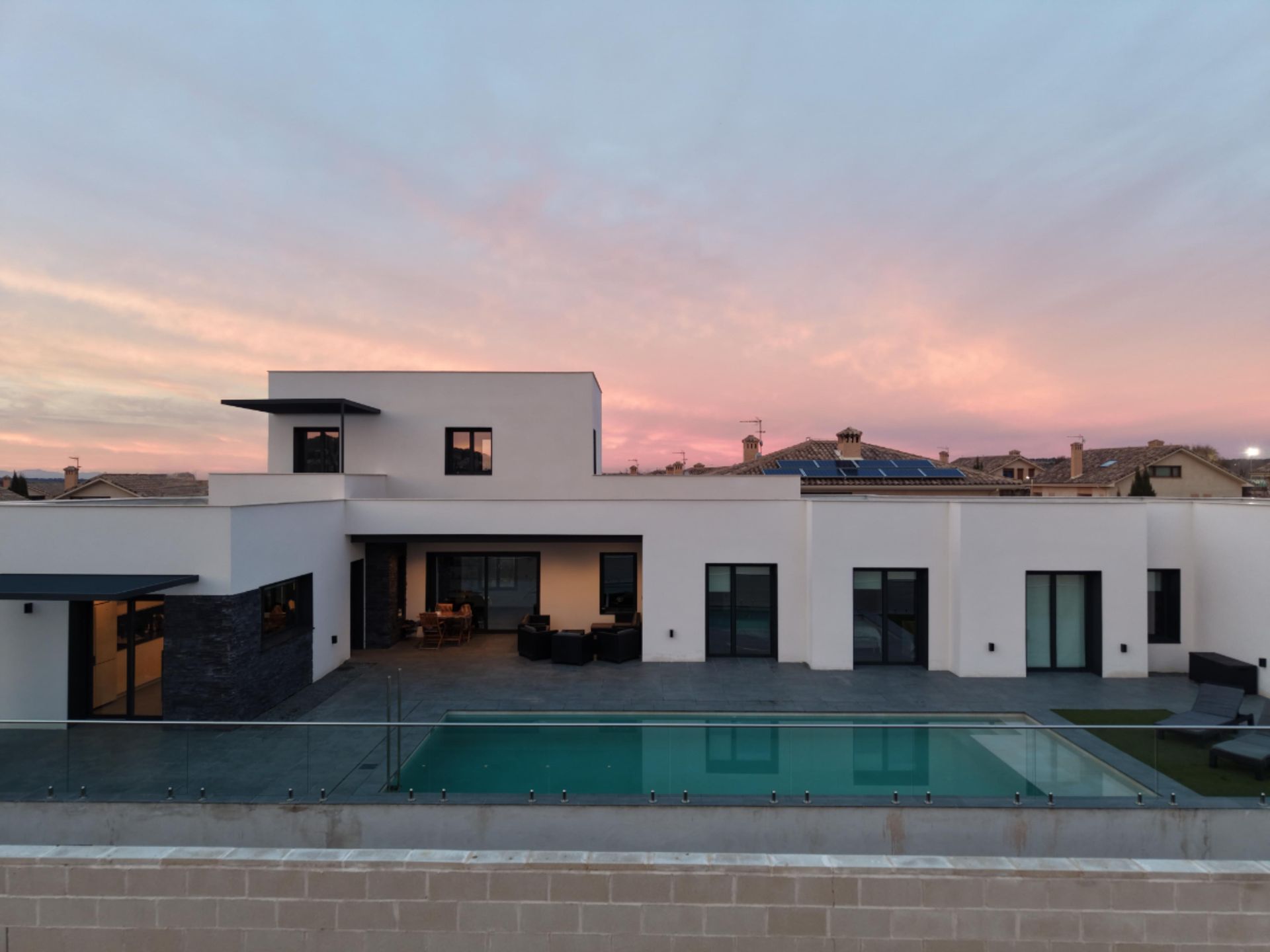 Moderna casa blanca con piscina, patio y cielo al atardecer.