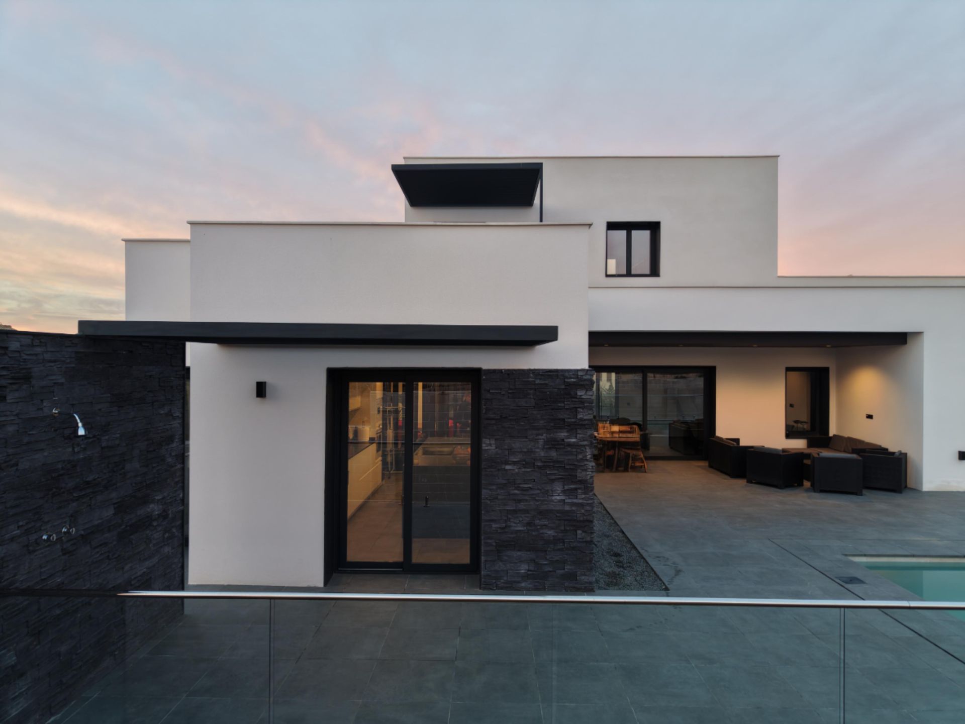 Casa blanca moderna con acentos oscuros, patio y piscina al anochecer.