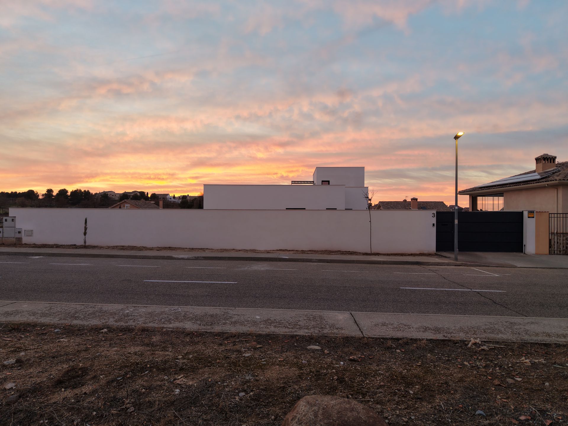 Carretera con pared blanca y edificio contra un cielo de atardecer colorido.