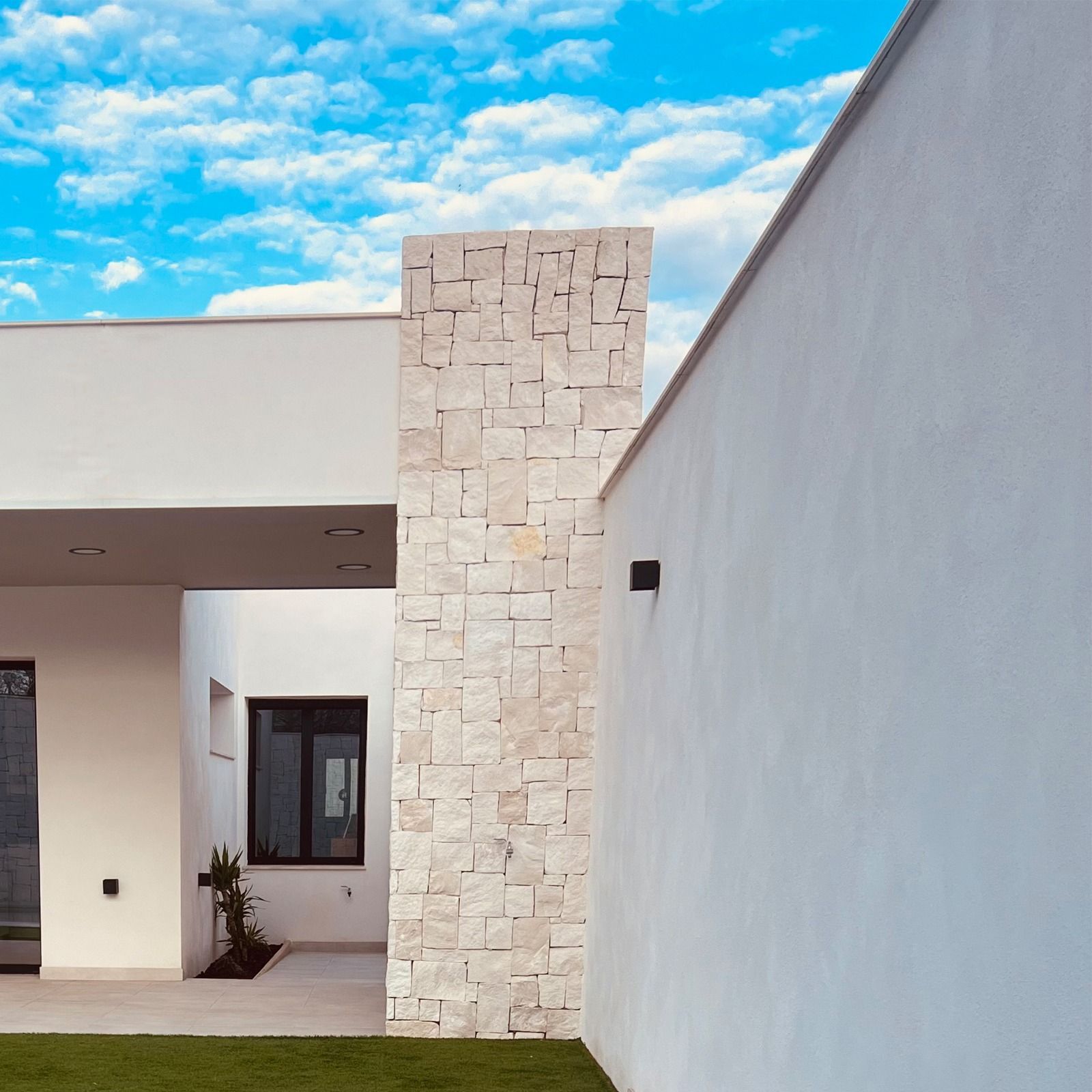 Exterior de edificio blanco moderno con pilares de piedra y cielo azul.