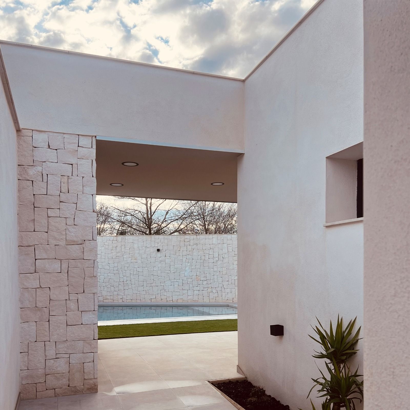 Exterior blanco moderno con piscina, pared con acento de piedra y cielo azul.
