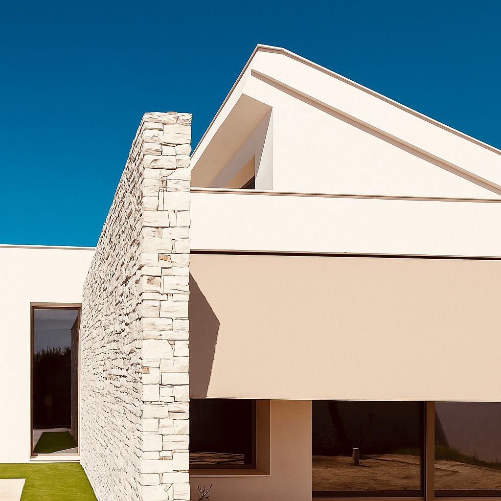 Casa blanca moderna con pared de piedra, toldo beige y grandes ventanales contra un cielo azul.