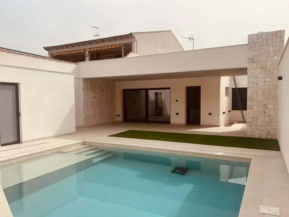 Vista de la piscina de una casa blanca moderna con una piscina rectangular, césped artificial y una pared con acento de piedra.