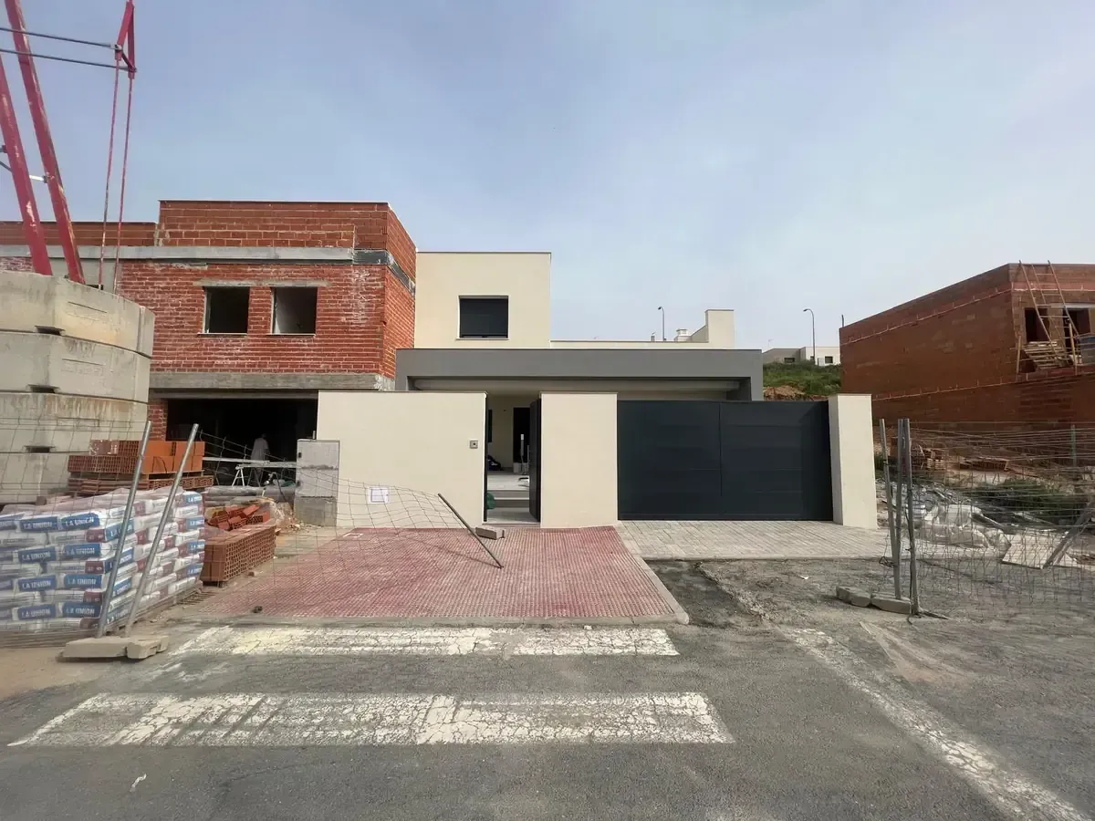 Casa moderna en construcción con ladrillo y acentos grises, portón negro y pavimento rojo.