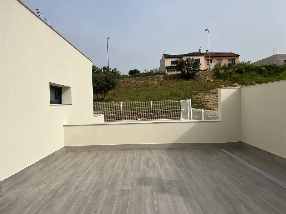 Patio exterior con piso imitación madera gris claro, paredes blancas y vista a una ladera con casas.