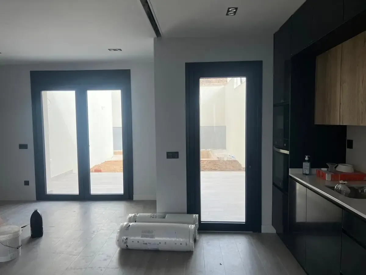 Vista interior de una casa moderna con puertas abiertas a un patio. Puertas y gabinetes de cocina con marco negro.