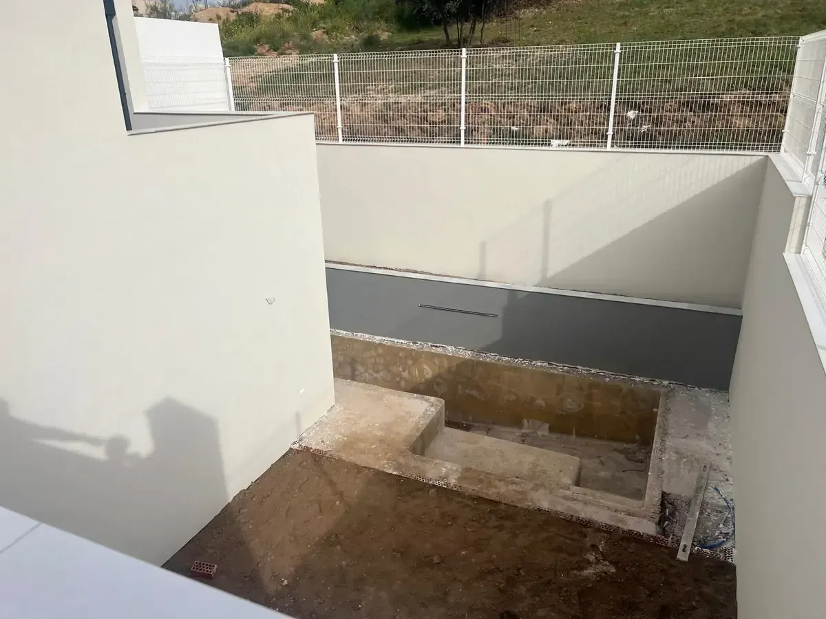 Un patio de hormigón hundido con escaleras. Se ven paredes de color gris claro y una valla blanca.