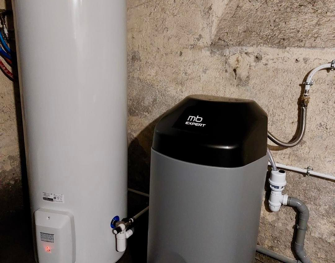 Adoucisseur d'eau et chauffe-eau dans un sous-sol avec mur de béton apparent.