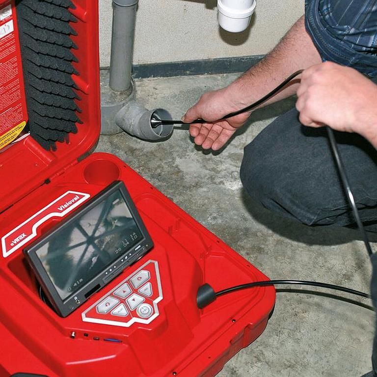 Plombier utilisant une caméra d'inspection d'égout pour observer l'intérieur d'une canalisation. Boîte à outils rouge avec écran posé au sol.