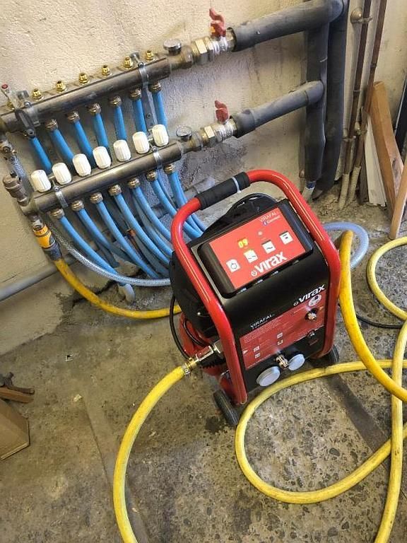 Machine rouge reliée à des tuyaux bleus pour un test de pression dans un sous-sol.