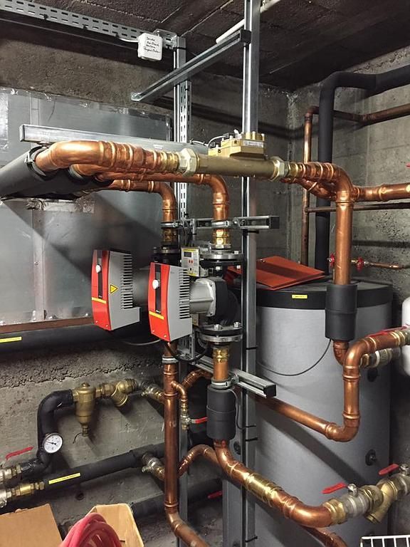 Tuyaux en cuivre et équipement de chauffage dans une buanderie contre un mur en béton.