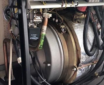 Vue intérieure d'une chaudière à gaz, montrant des tuyaux, des vannes et un réservoir d'eau cylindrique enveloppé d'isolant.