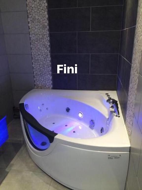 Jacuzzi d'angle avec lumières bleues et violettes dans une salle de bain moderne.