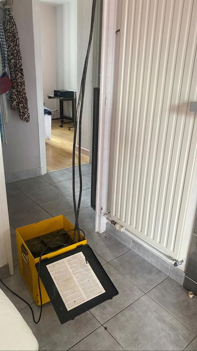 Boîte jaune avec équipement à côté d'un radiateur dans un couloir, câbles électriques au-dessus.