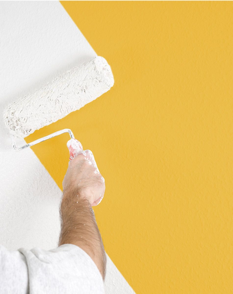 Un ouvrier repeint un mur jaune en blanc