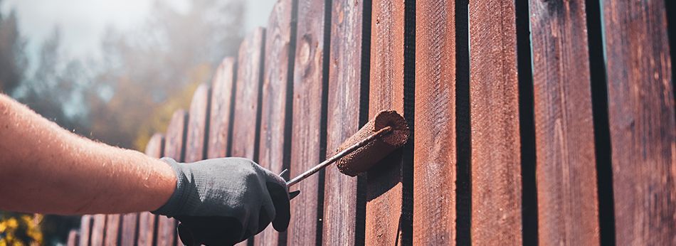 Une personne repeint une clôture en bois