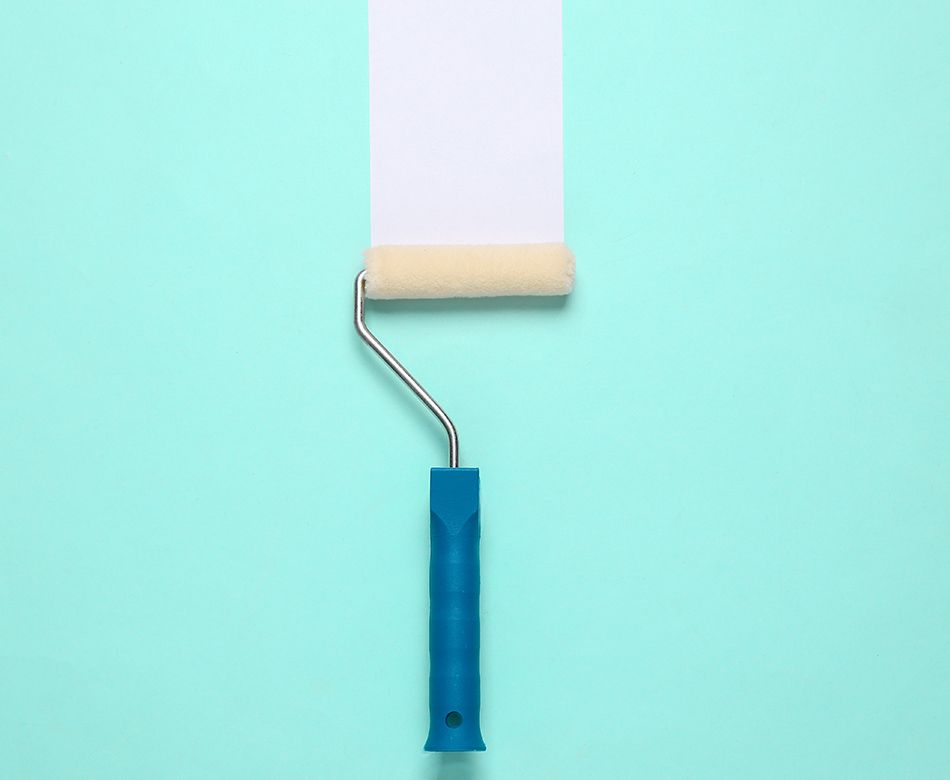 Un pinceau rouleau avec une peinture blanche sur un mur bleue clair