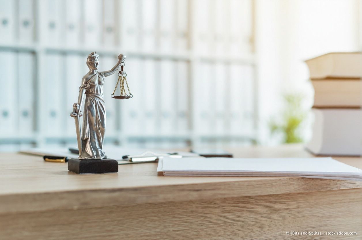 Statue der Justitia auf einem Schreibtisch mit Waage und Schwert, juristischen Dokumenten und Büchern in einer Büroumgebung.