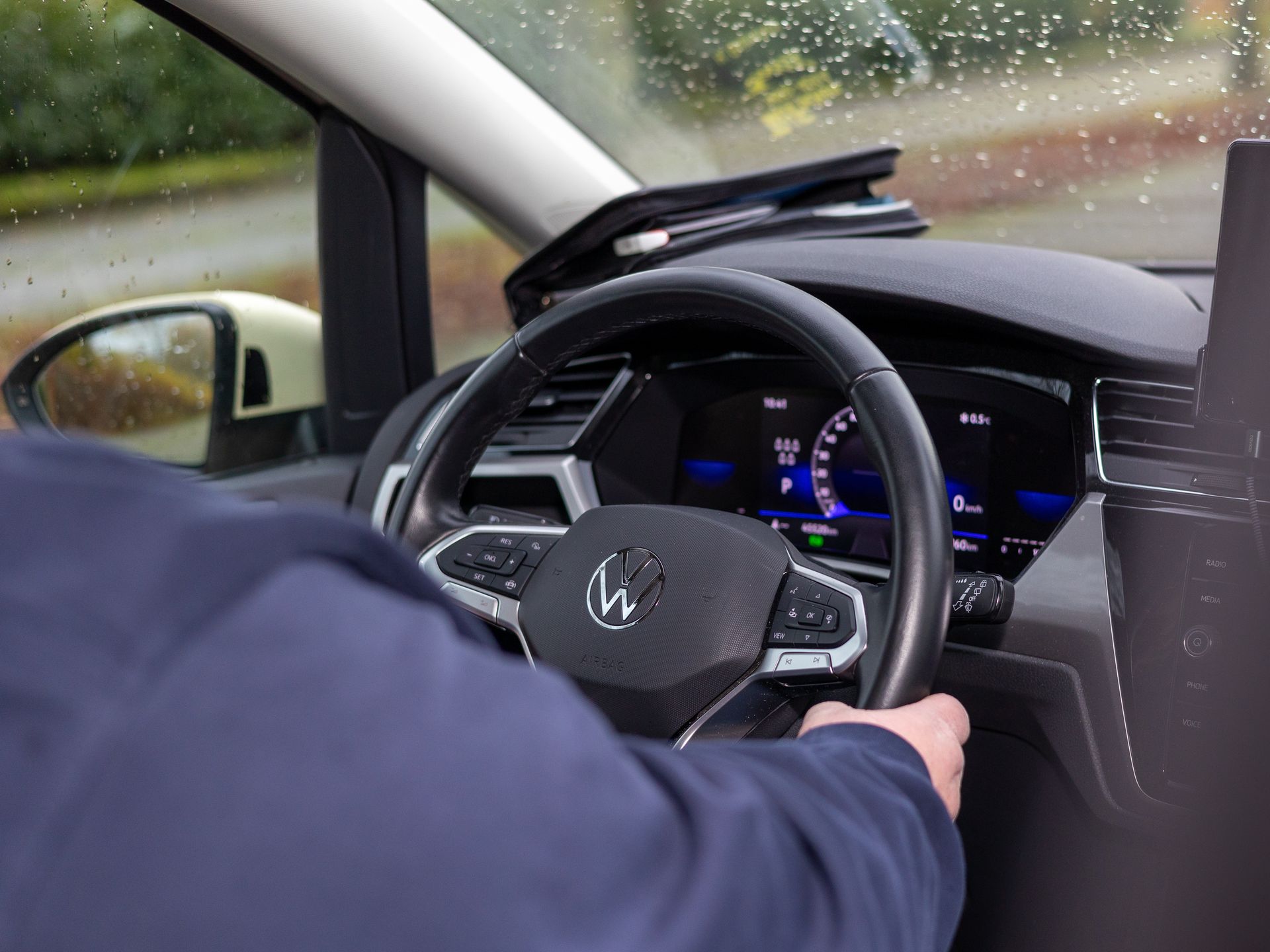 Eine Person fährt ein Auto mit dem Buchstaben W auf dem Lenkrad.