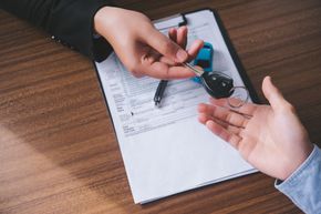 Persona entregando las llaves del coche a otra persona sobre un contrato en un escritorio de madera.