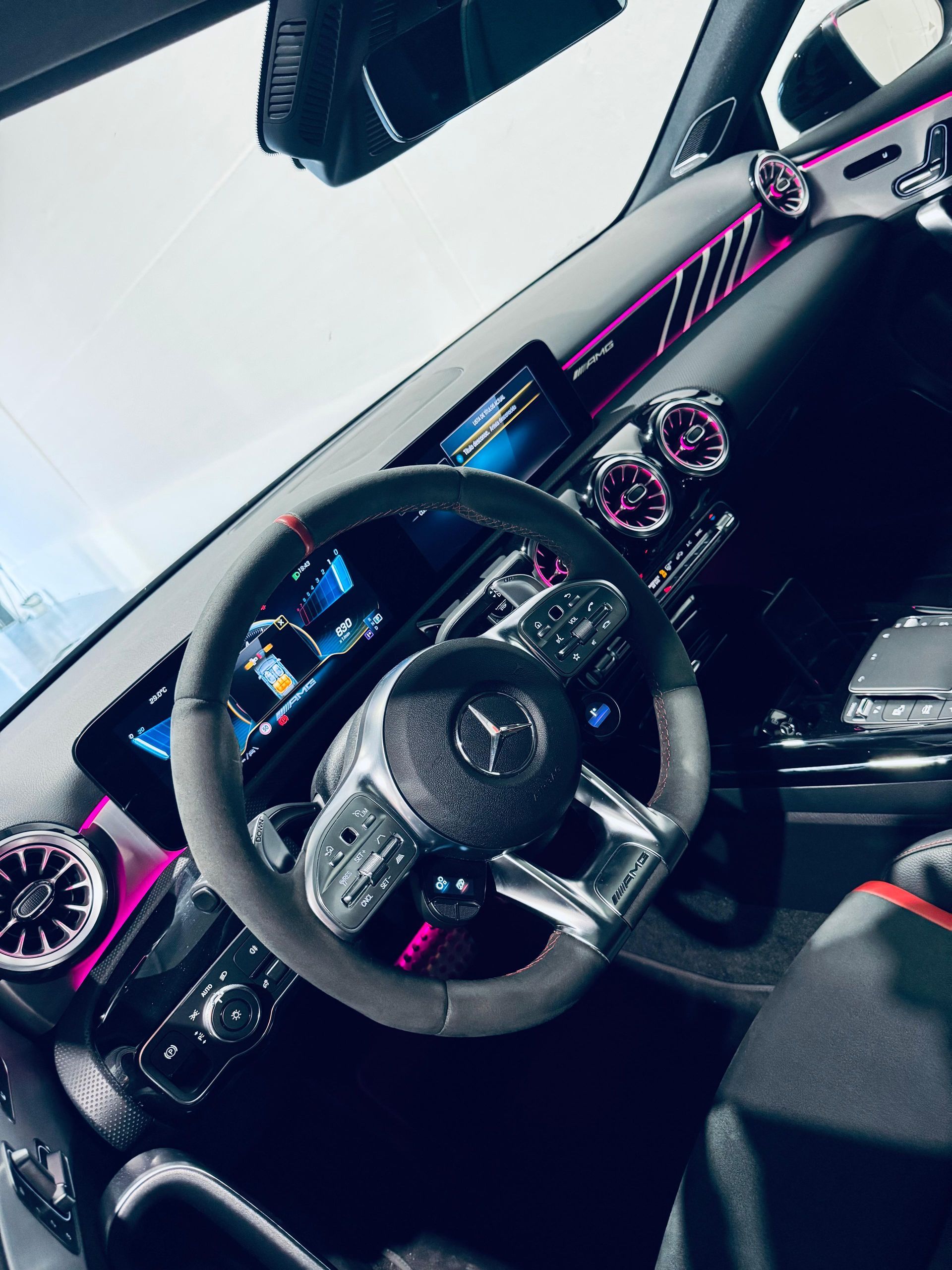 Dos mecánicos con monos azules y un cliente con chaqueta blanca inspeccionan el motor de un coche rojo.