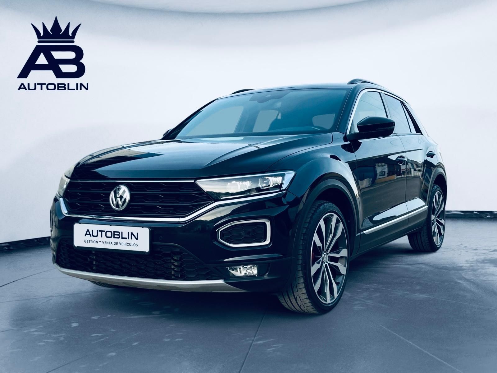 Primer plano del faro de un coche gris oscuro, otro SUV blanco con un lazo rojo al fondo, en una sala de exposición de automóviles.